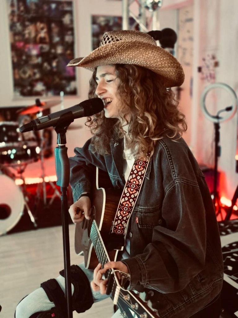 Amy singt mit Cowboyhut und Gitarre